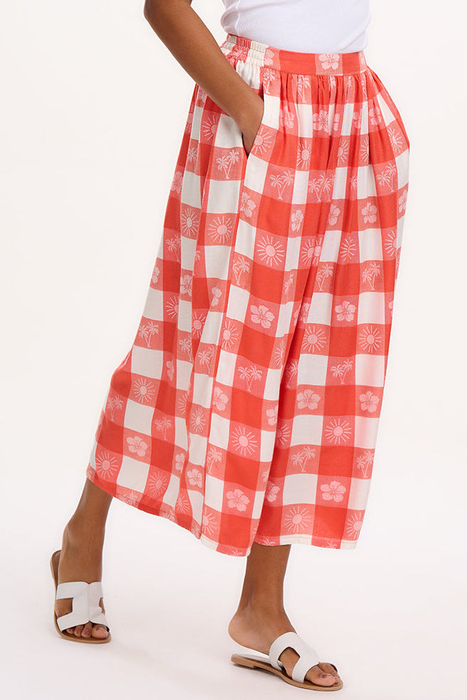 A model wearing an off-white and coral tropical gingham skirt with a fitted waistband and side pockets.