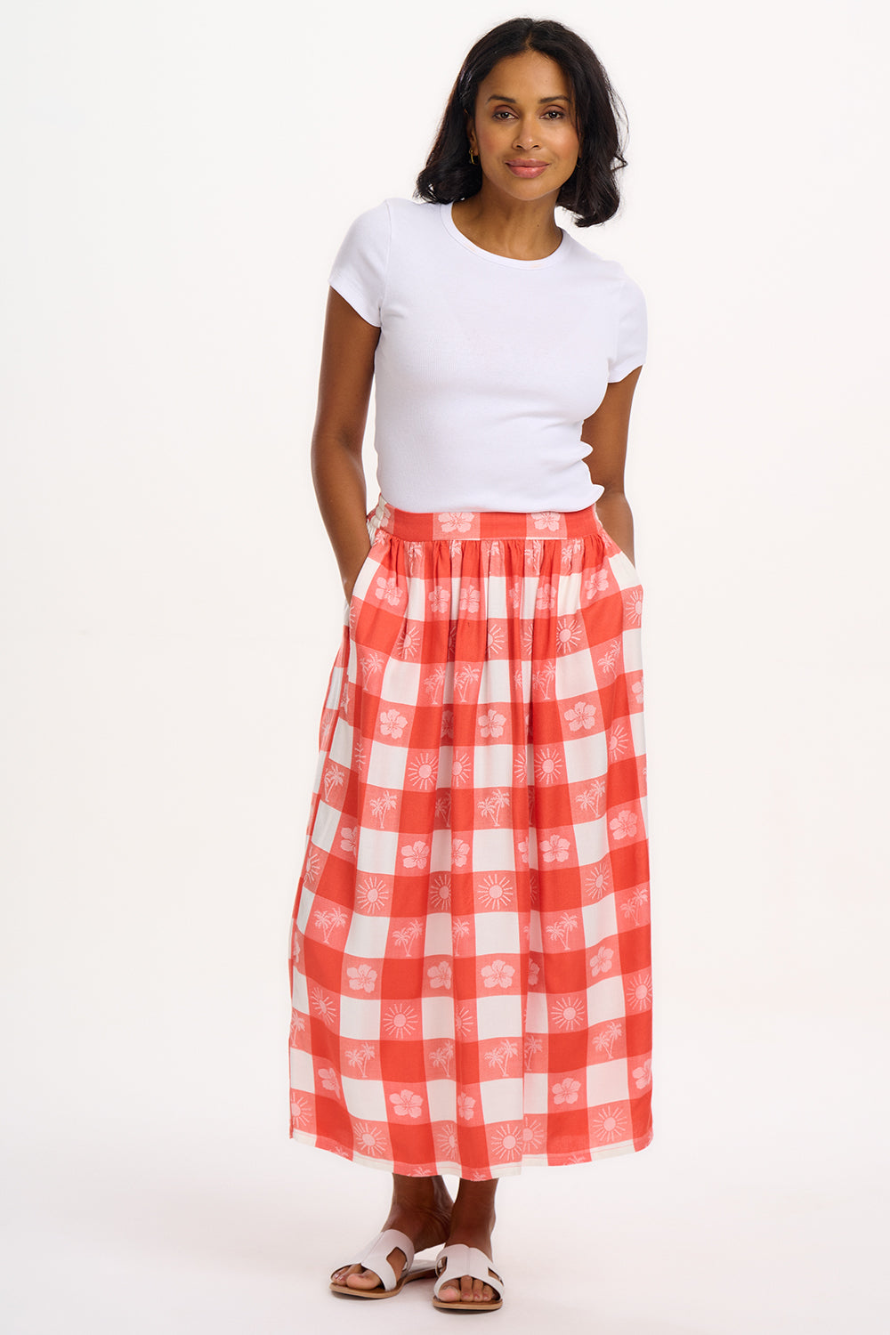 A model wearing an off-white and coral tropical gingham skirt with a fitted waistband and side pockets.
