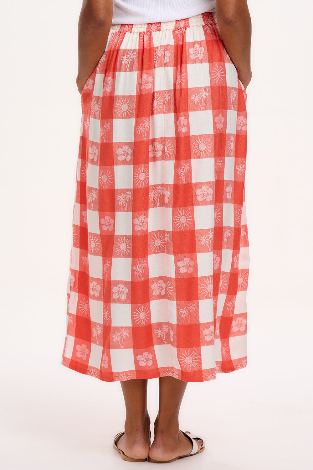 A model wearing an off-white and coral tropical gingham skirt with a fitted waistband and side pockets.