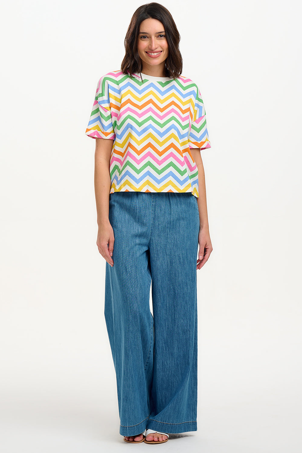 A woman smiling and wearing a multicolored t-shirt with a zigzag rainbow stripe design and short sleeves.