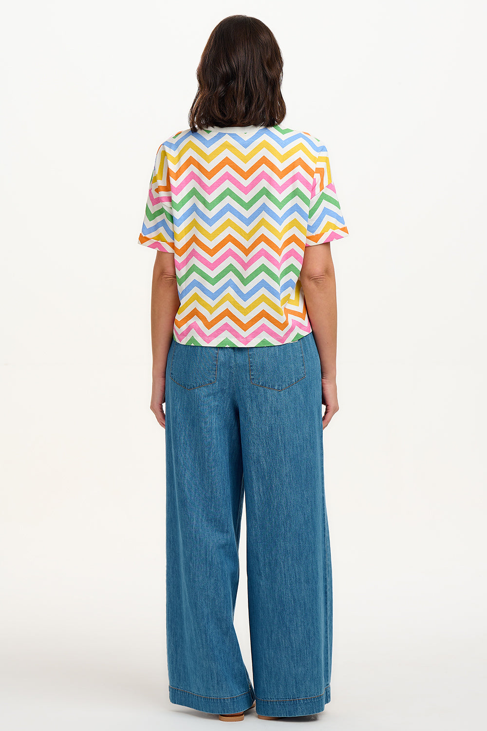 A woman smiling and wearing a multicolored t-shirt with a zigzag rainbow stripe design and short sleeves.