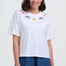 Woman wearing a white t-shirt with colorful floral embroidery on a plain background