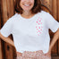 Woman wearing a white t-shirt with red heart pattern and leopard print pants standing against a wooden background