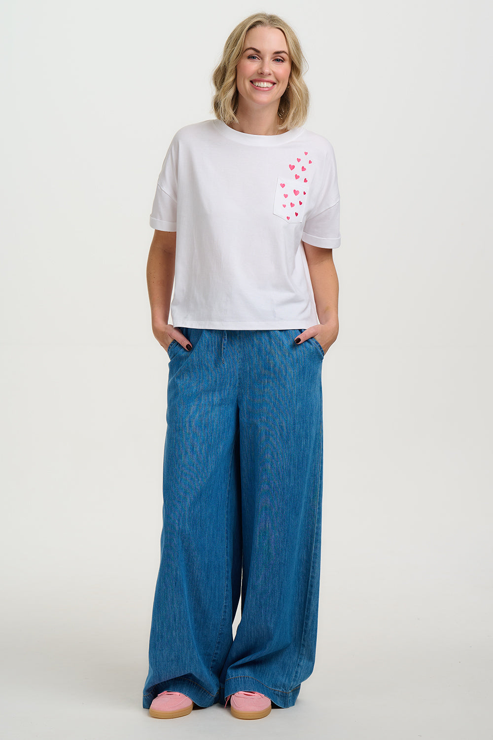 Woman wearing a white t-shirt with a small design on the chest and blue wide-leg pants against a white background