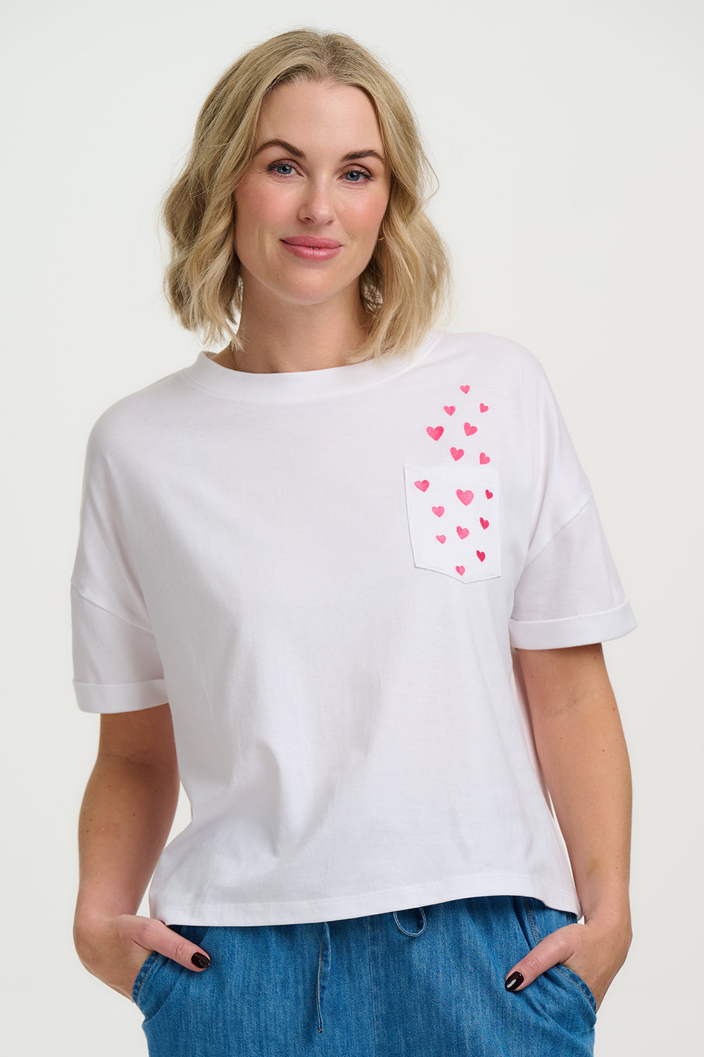 Woman wearing a white t-shirt with pink heart designs on a plain background