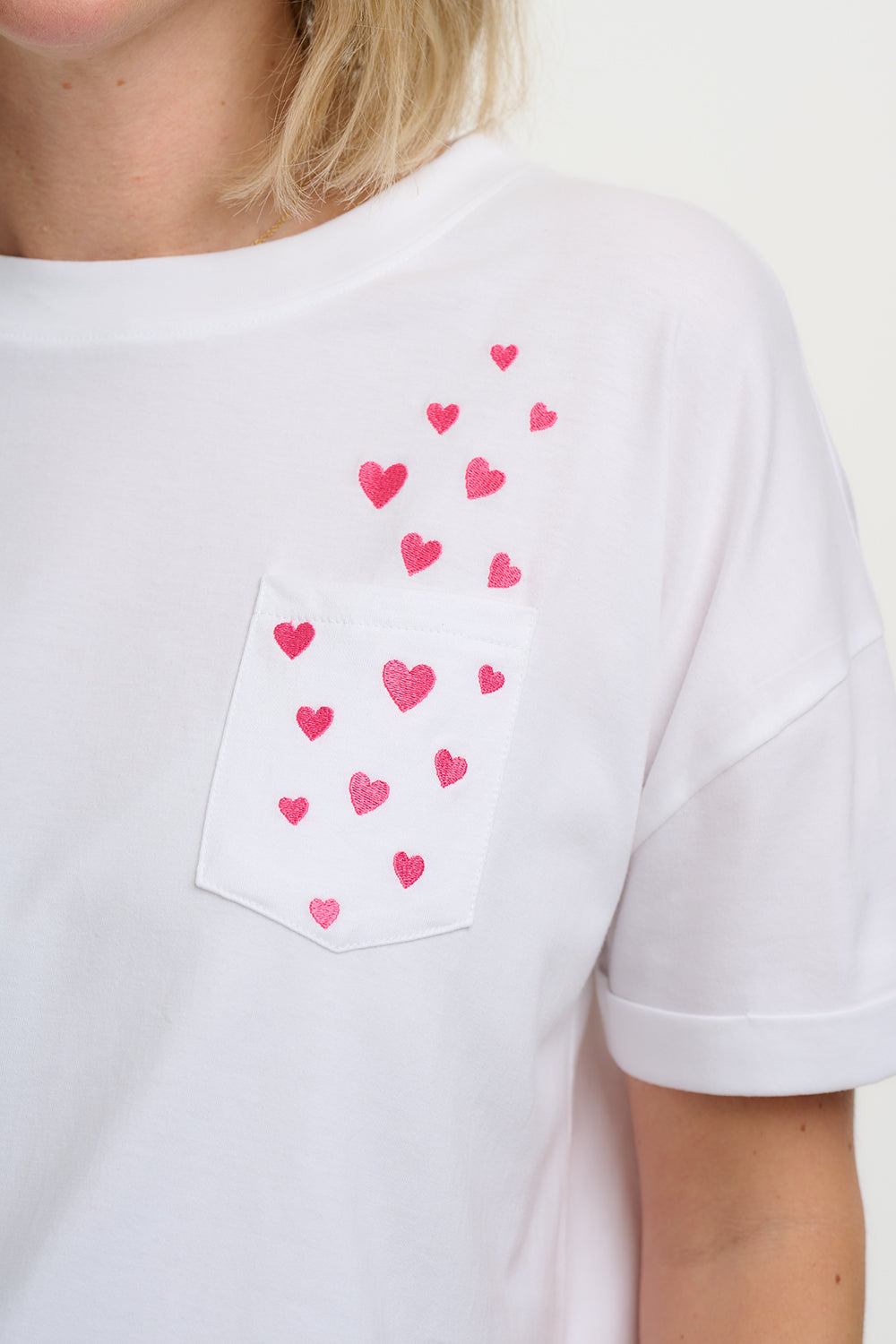 White t-shirt with pink heart patterns on a plain background