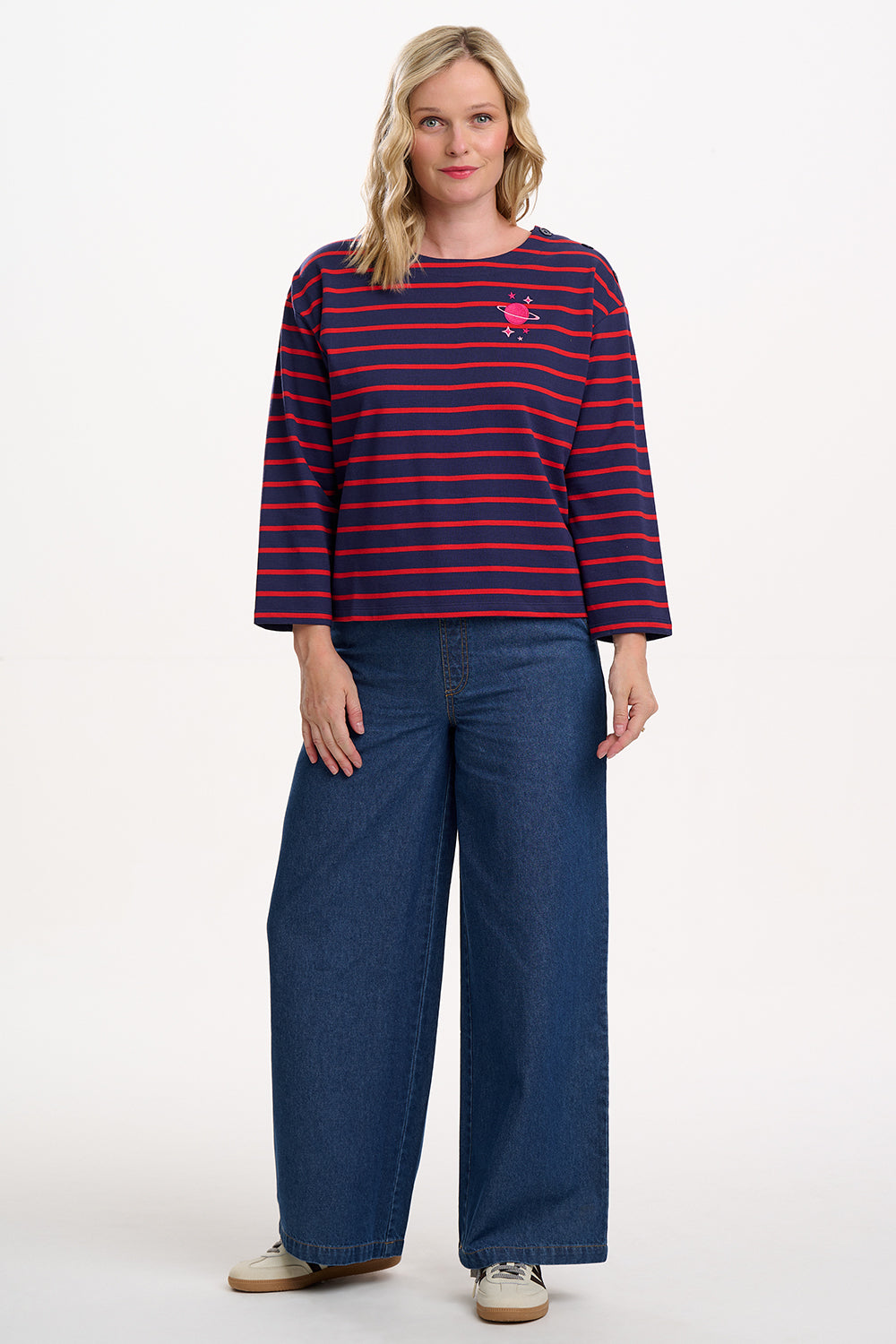 Sugarhill Brighton model wearing a red and blue striped shirt with a logo and blue jeans on a white background