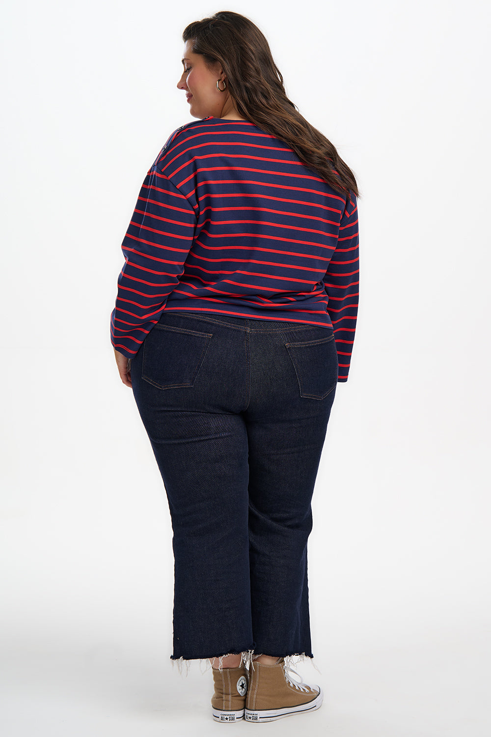 Person wearing a red and blue striped shirt and dark jeans on a white background