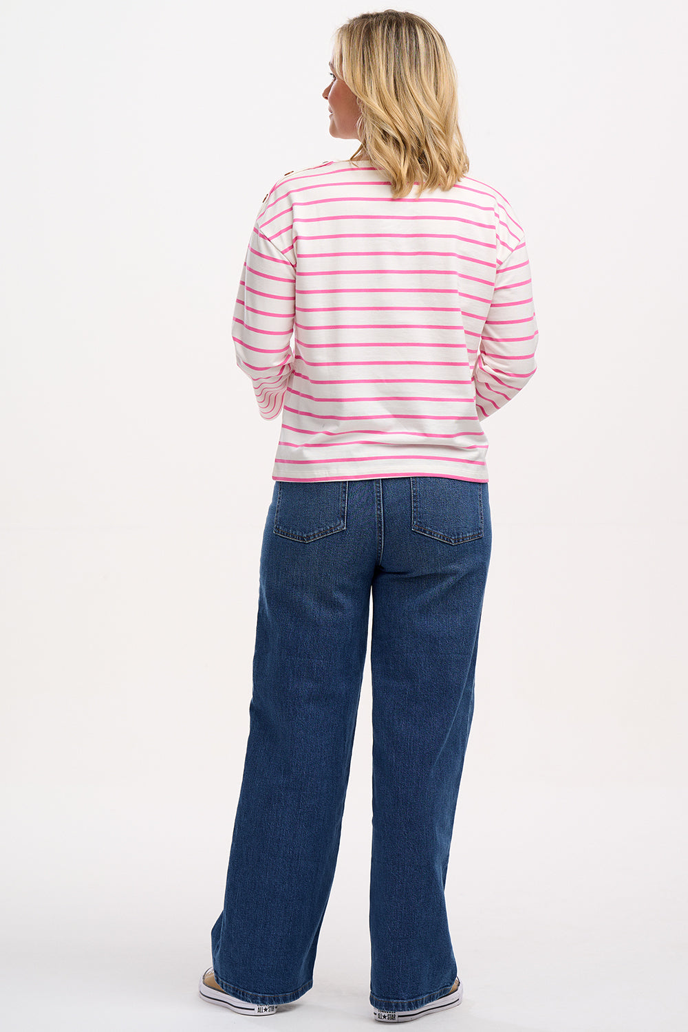 A woman wearing an off-white and pink striped Breton top with a smiley flower embroidery on the chest, paired with jeans.