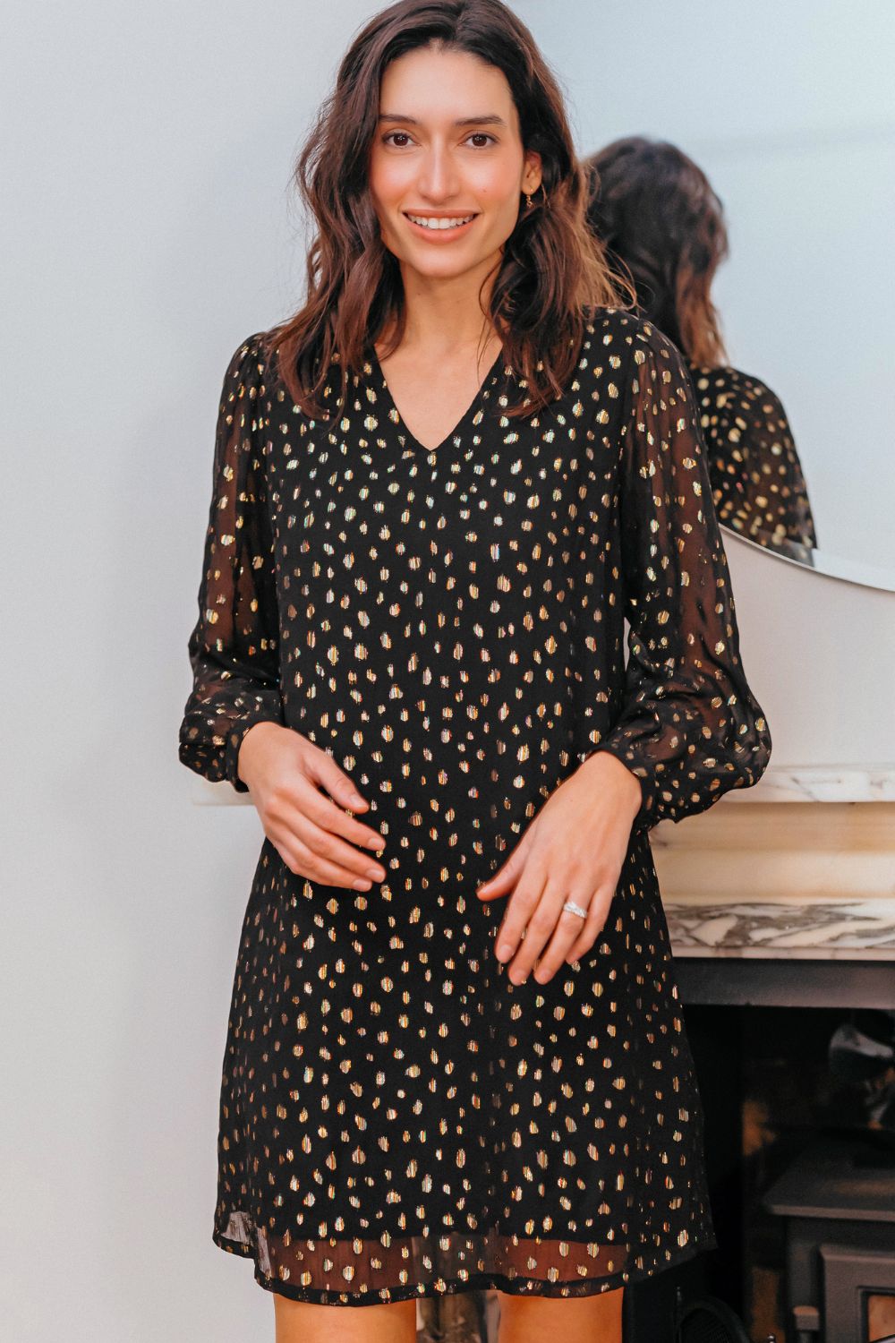 Woman wearing a black dress with gold polka dots indoors.