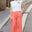 Woman wearing a white t-shirt with a logo and coral pants standing on a street.