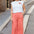 Woman wearing a white t-shirt with a logo and coral pants standing on a street.