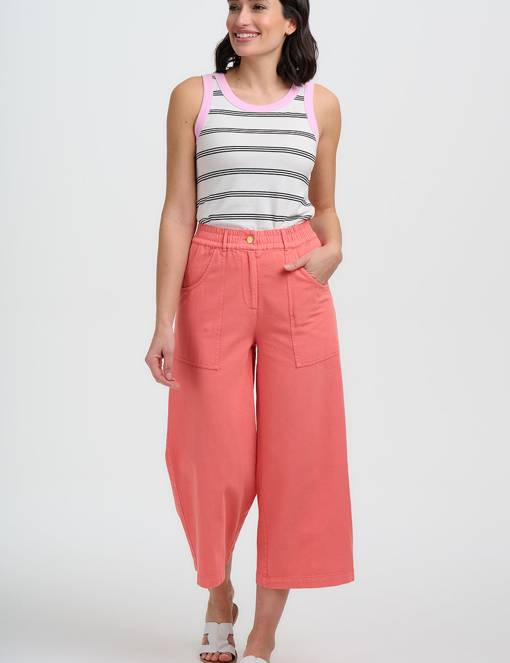 Woman wearing a striped tank top and coral pants on a white background