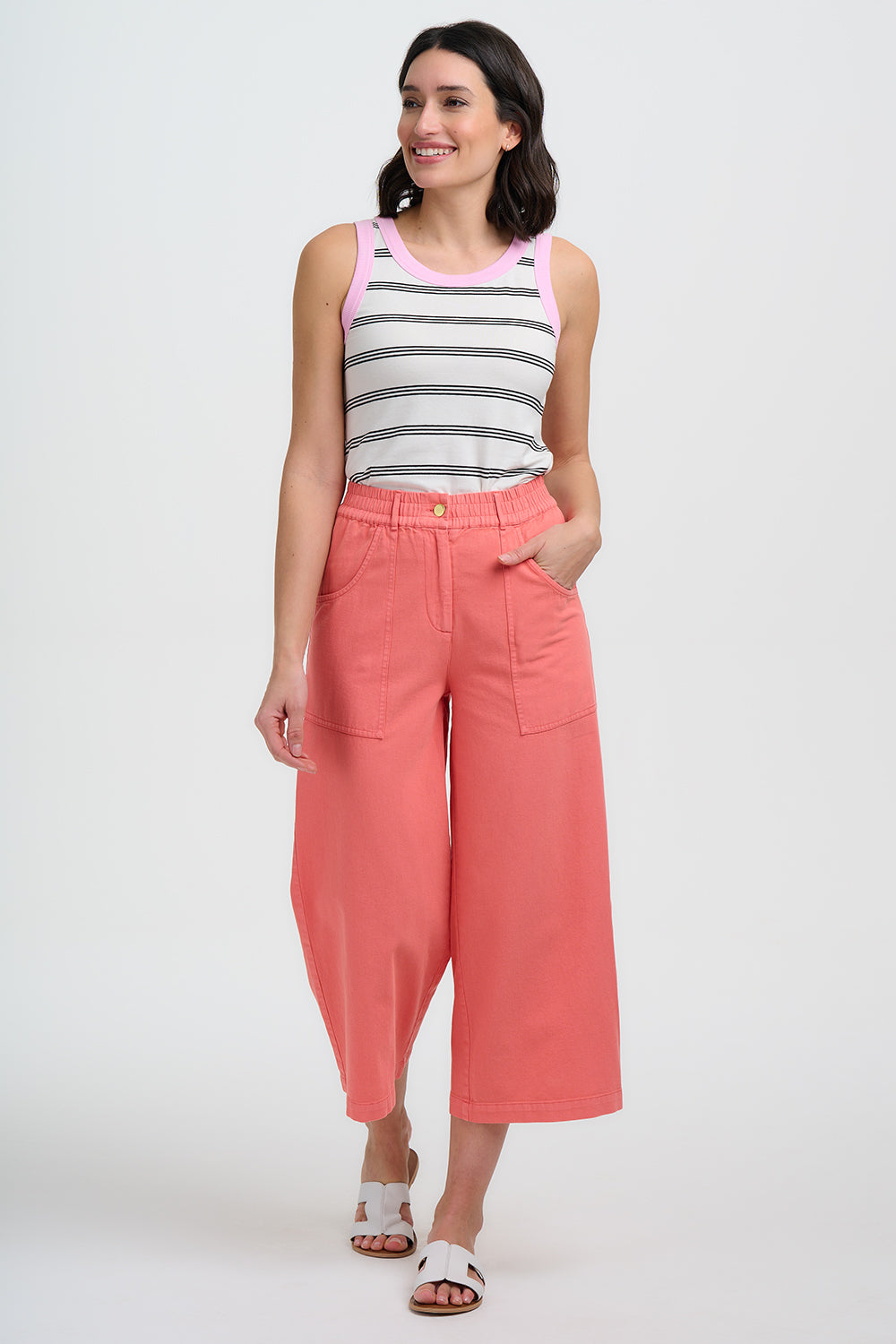 Woman wearing a striped tank top and coral pants on a white background