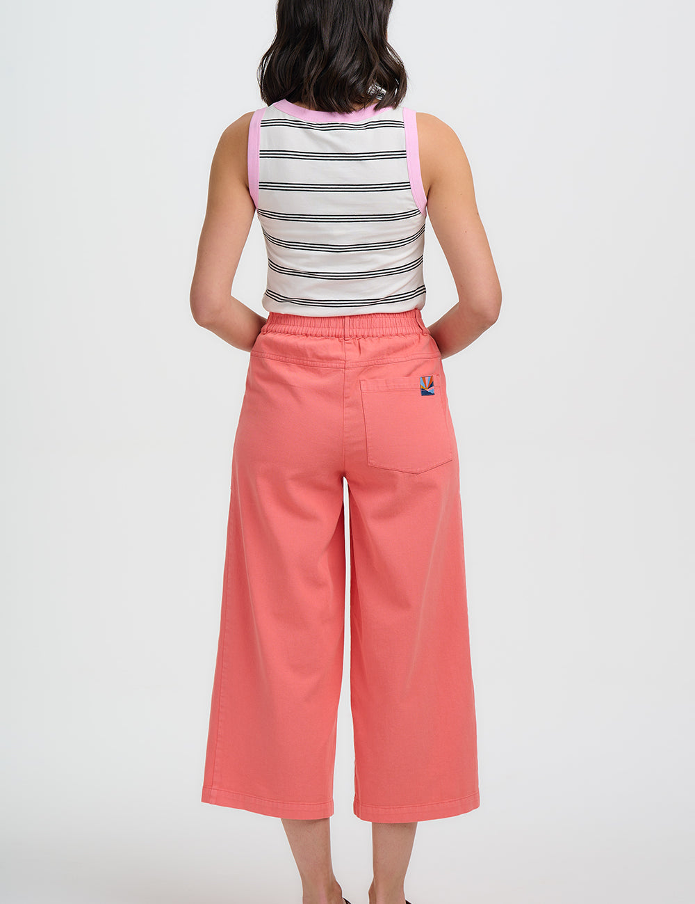 Woman wearing a striped sleeveless top and pink wide-leg pants on a white background