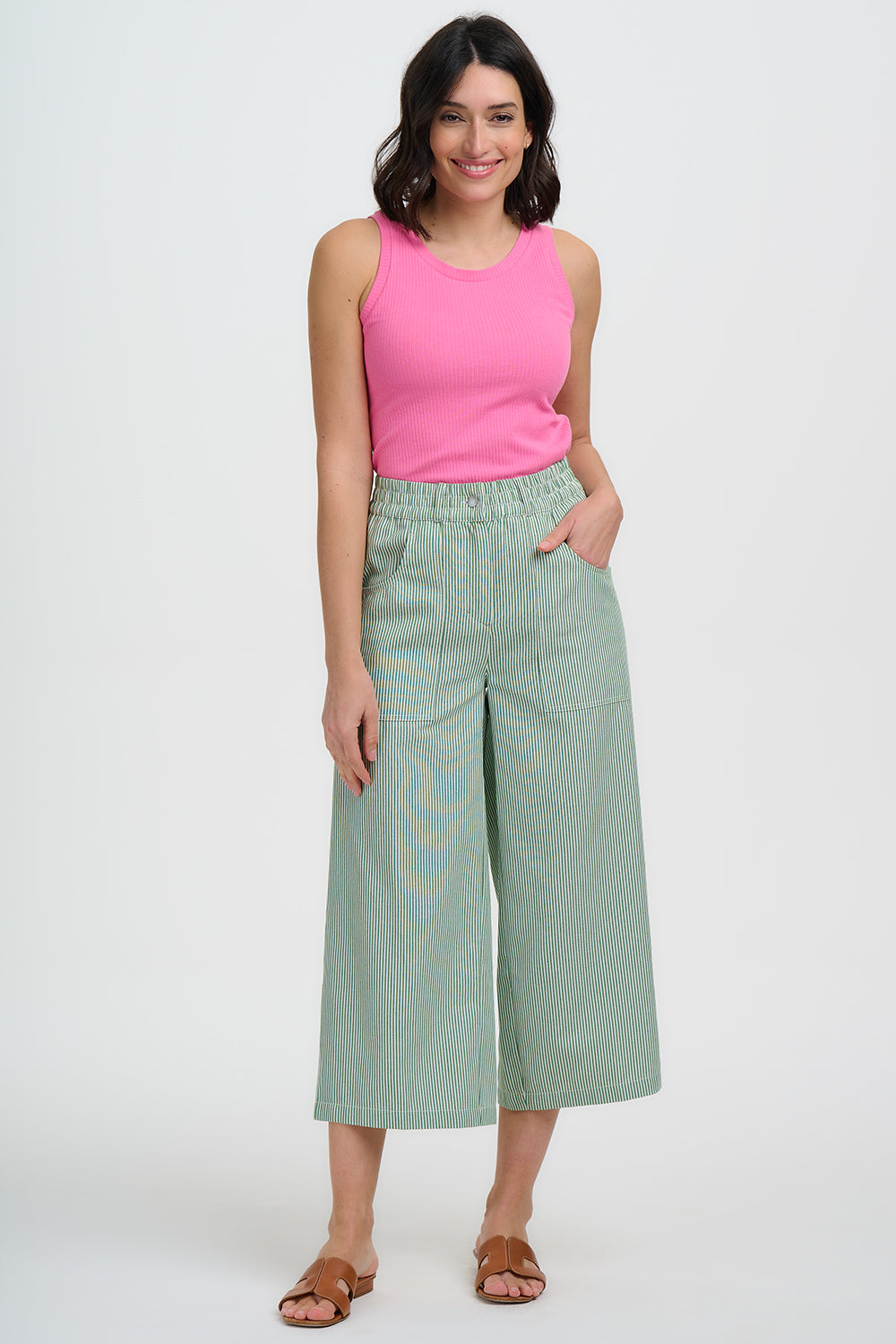 Woman wearing a pink sleeveless top and light green wide-leg pants on a white background