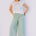 Woman wearing a colorful sleeveless top and light green pants against a plain background