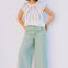 Woman wearing a colorful sleeveless top and light green pants against a plain background