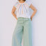 Woman wearing a colorful sleeveless top and light green pants against a plain background
