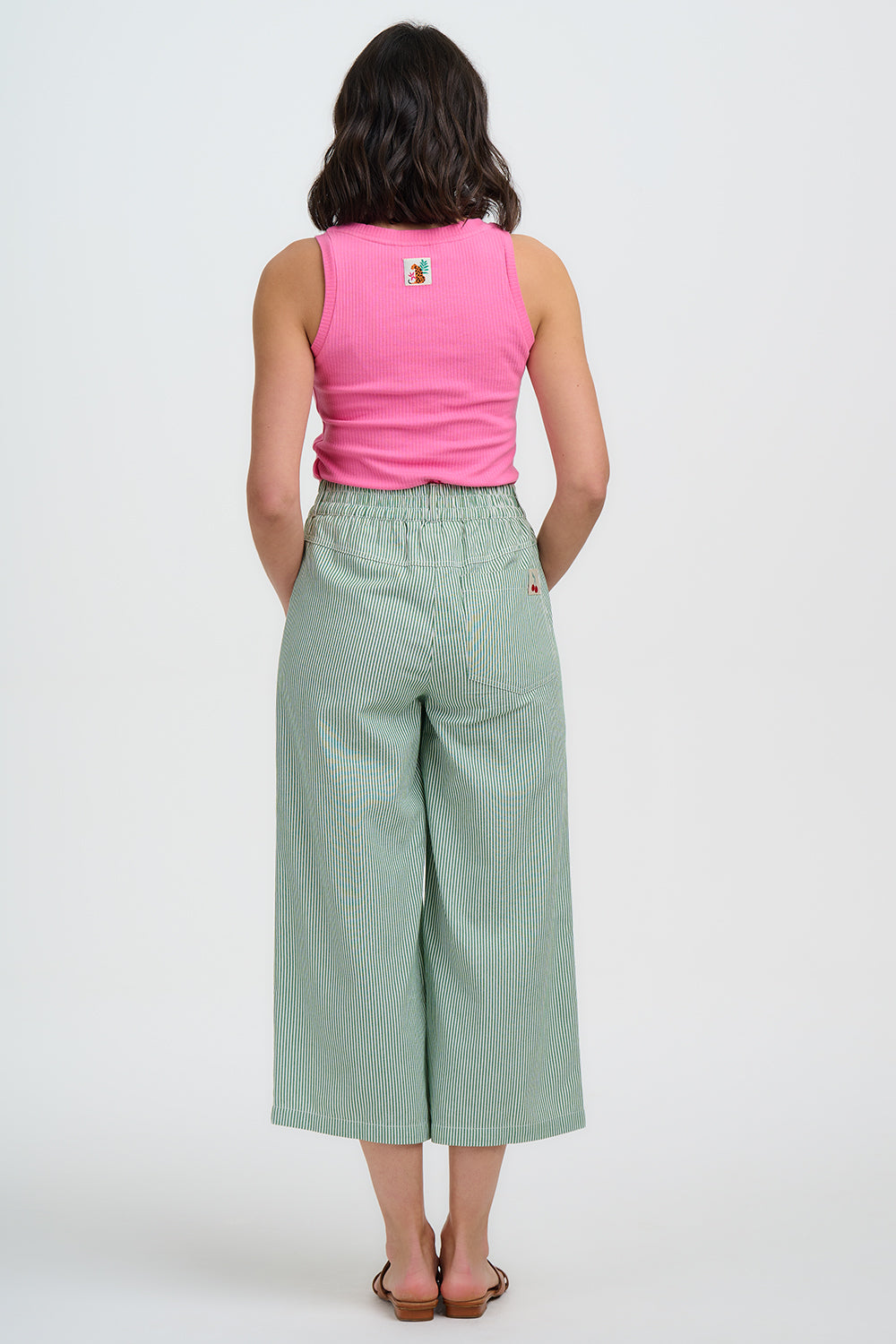 Person wearing a pink sleeveless top and light green wide-leg pants on a white background