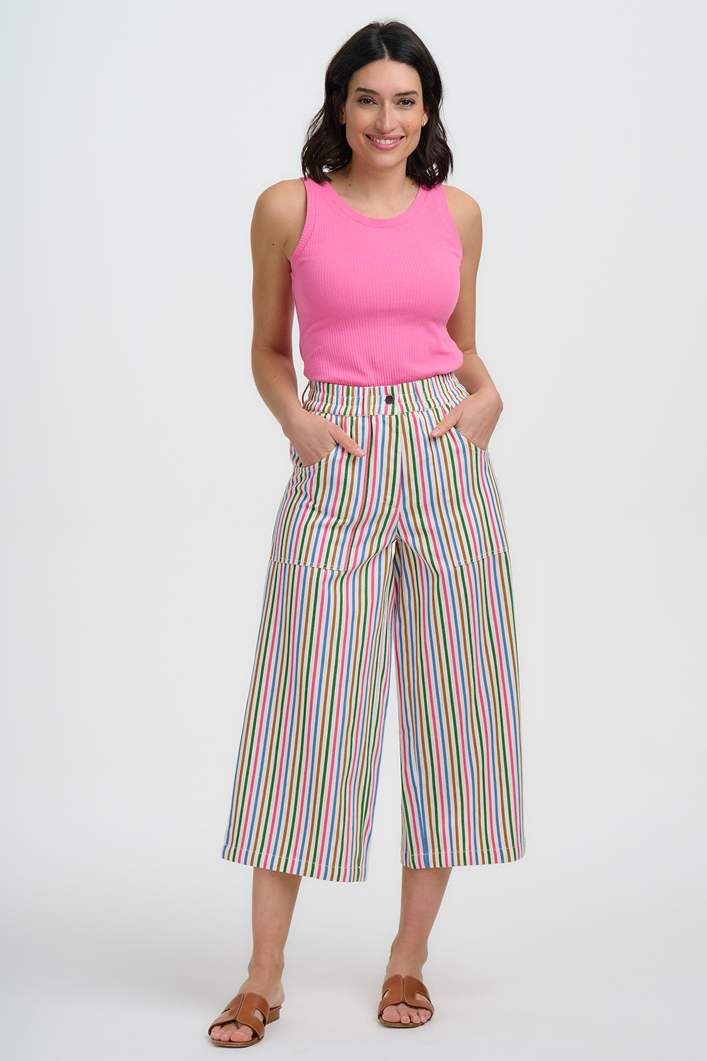 Woman wearing a pink sleeveless top and colorful striped pants on a white background