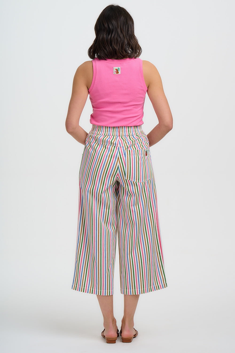 Person wearing a pink sleeveless top and colorful striped pants on a white background