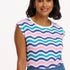 A woman smiling and wearing a sleeveless round neck t-shirt with a multicolored geometric pattern in shades of pink, green, and blue.