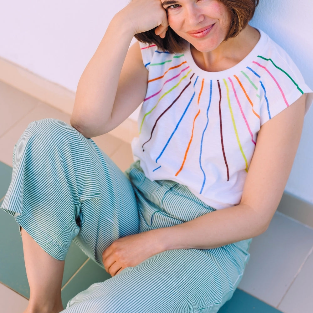 Woman wearing a colorful striped top and light blue pants sitting on a white surface.
