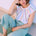 Woman wearing a colorful striped top and light blue pants sitting on a white surface.