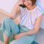 Woman wearing a colorful striped top and light blue pants sitting on a white surface.