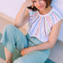 Woman wearing a colorful striped top and light blue pants sitting on a white surface.