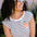 A woman smiling and wearing a sleeveless striped white and navy t-shirt with an embroidered orange on the chest.