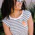 A woman smiling and wearing a sleeveless striped white and navy t-shirt with an embroidered orange on the chest.