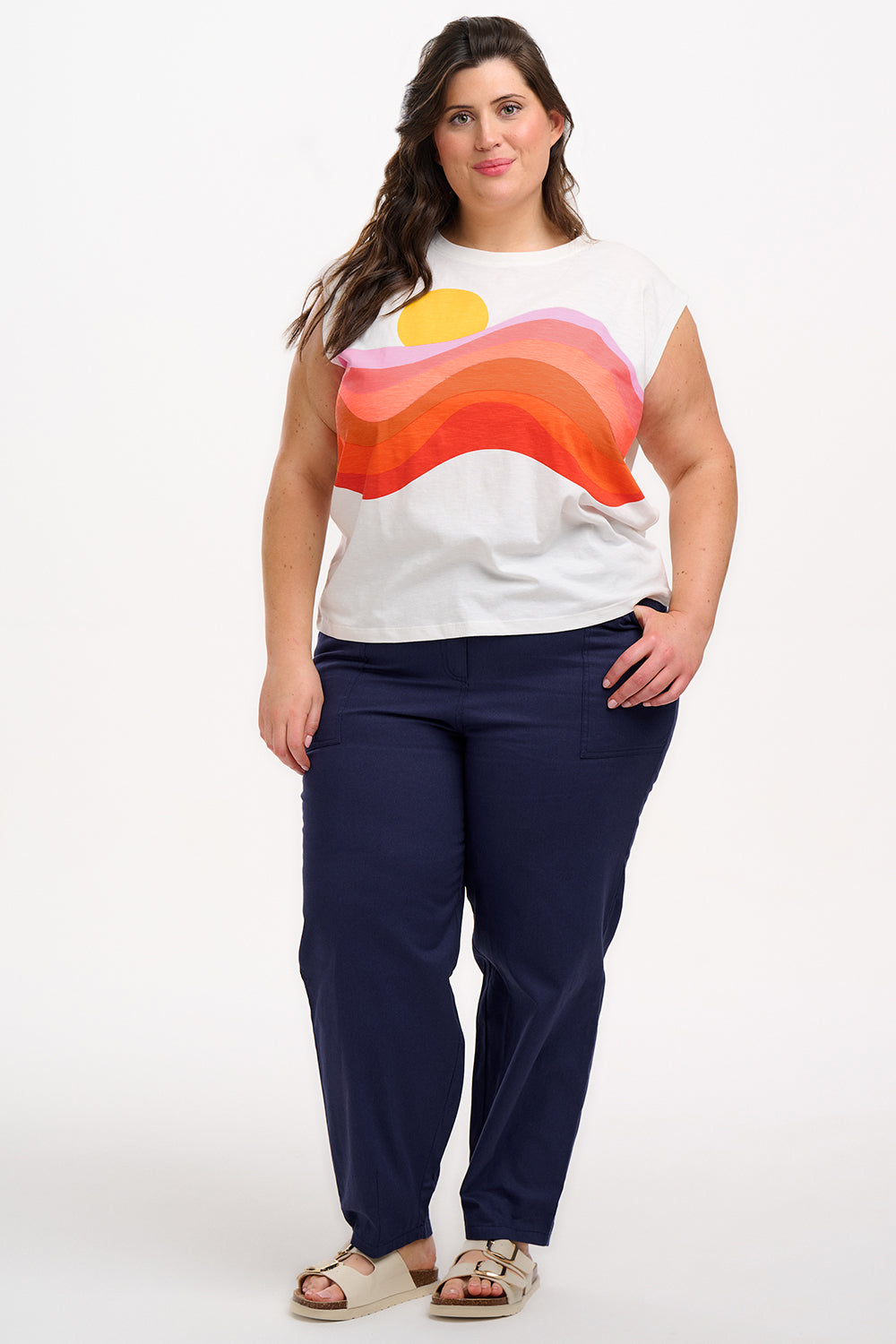 Woman wearing a colorful sleeveless top and navy pants on a white background