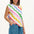 A woman modeling a sleeveless t-shirt with a geometric pattern of rainbow-colored waves on an off-white background.