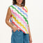 A woman modeling a sleeveless t-shirt with a geometric pattern of rainbow-colored waves on an off-white background.