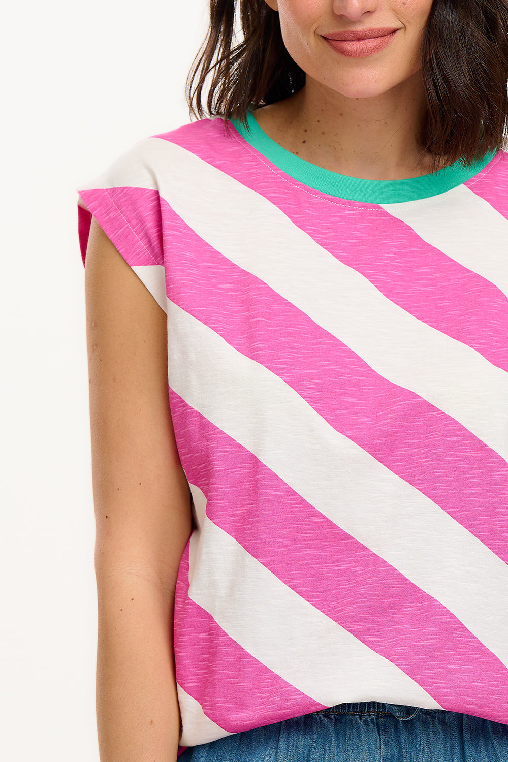 Sugarhill Brighton t-shirt. A female model wearing an oversized sleeveless striped t-shirt in pink and white, paired with blue jeans.