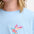 A woman wearing a pale blue sleeveless t-shirt with a tropical hummingbird graphic on the front