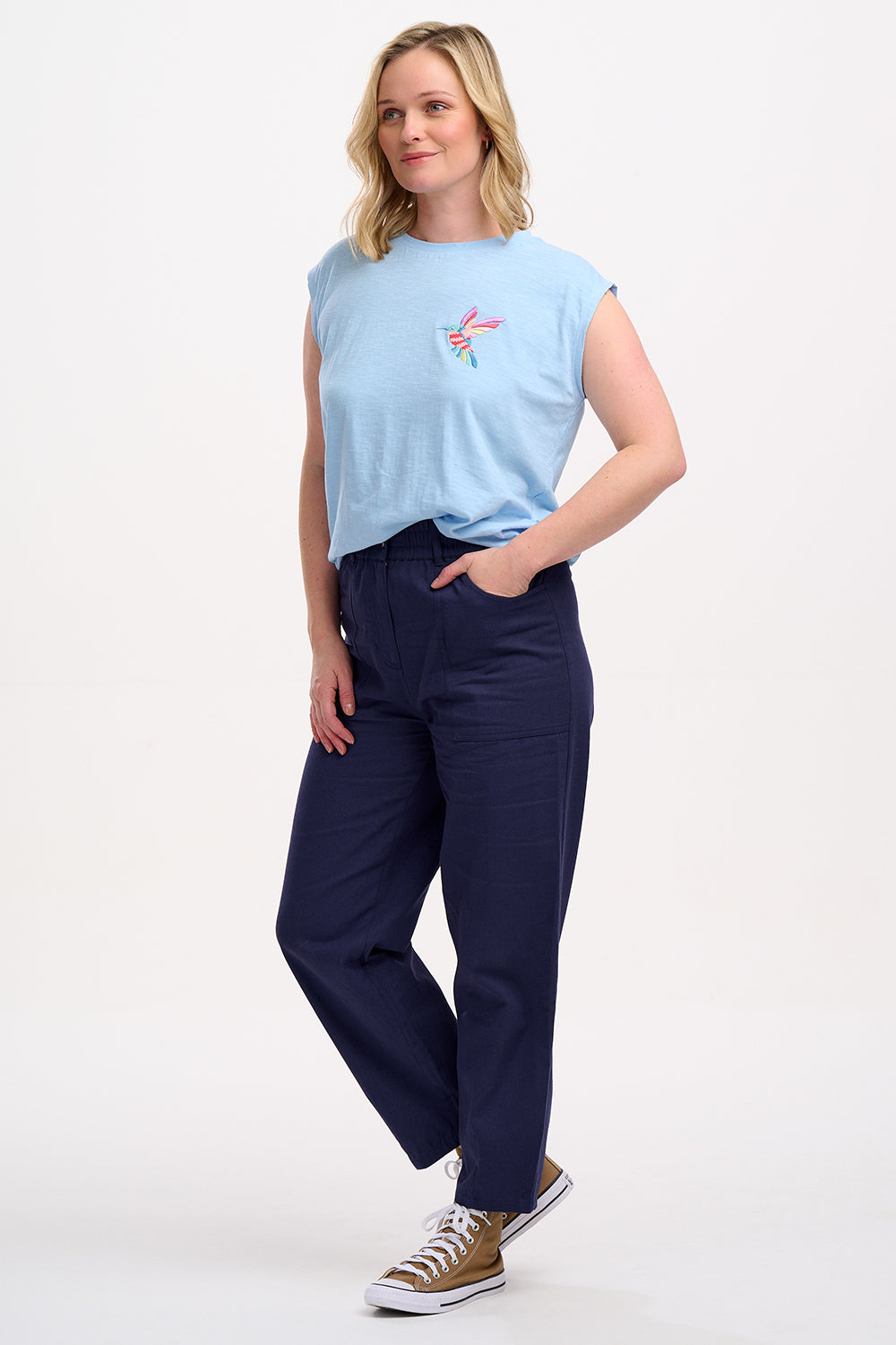 A woman wearing a pale blue sleeveless T-shirt with a tropical hummingbird graphic on the front.