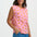 Woman wearing a pink sleeveless top with orange fruit pattern and blue pants on a white background