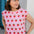 Woman wearing a pink t-shirt with strawberry pattern and a white cap.