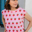 Woman wearing a pink t-shirt with strawberry pattern and a white cap.