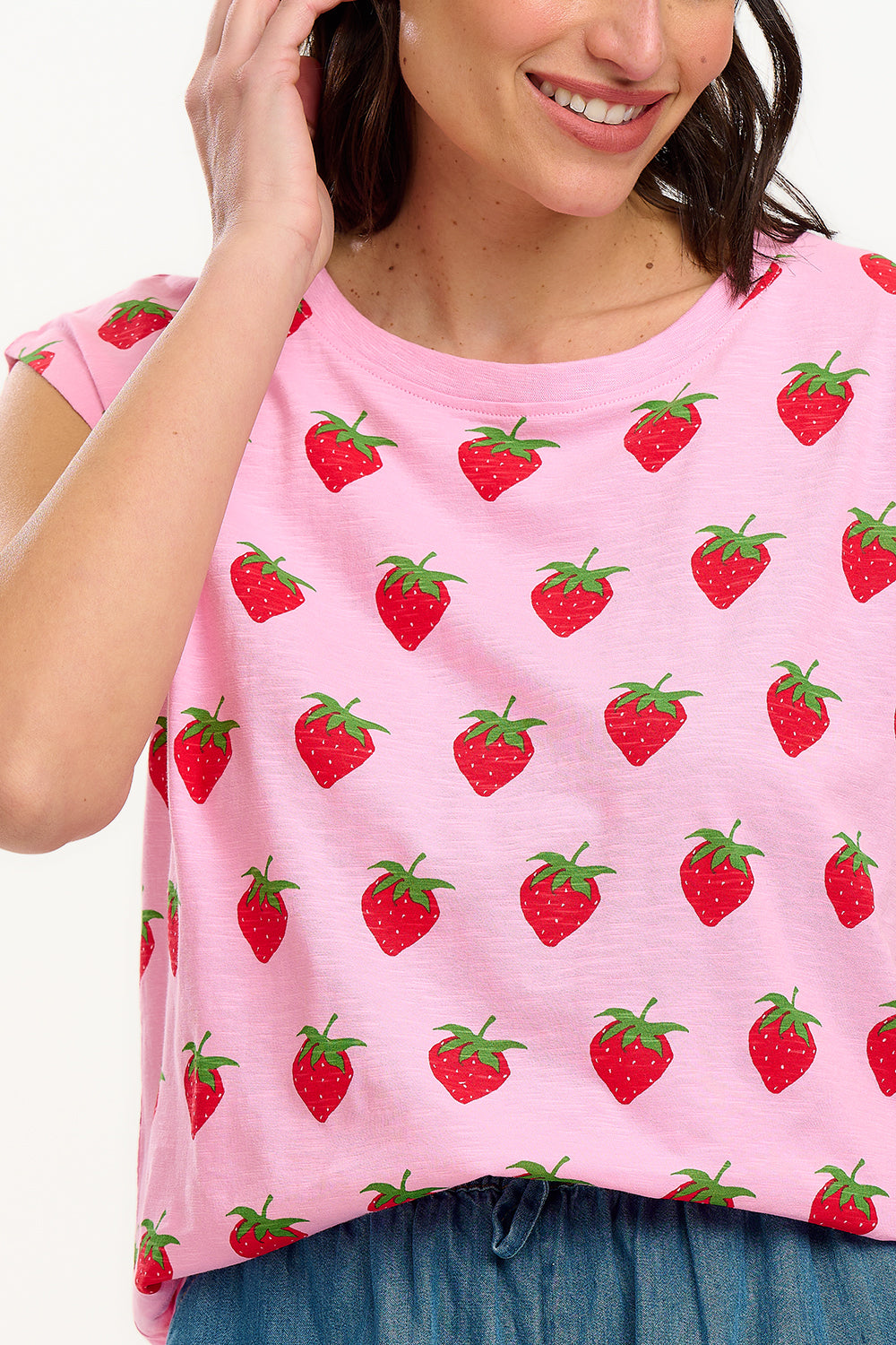 A model wearing a pink sleeveless tank top with a strawberry print, paired with blue denim shorts.
