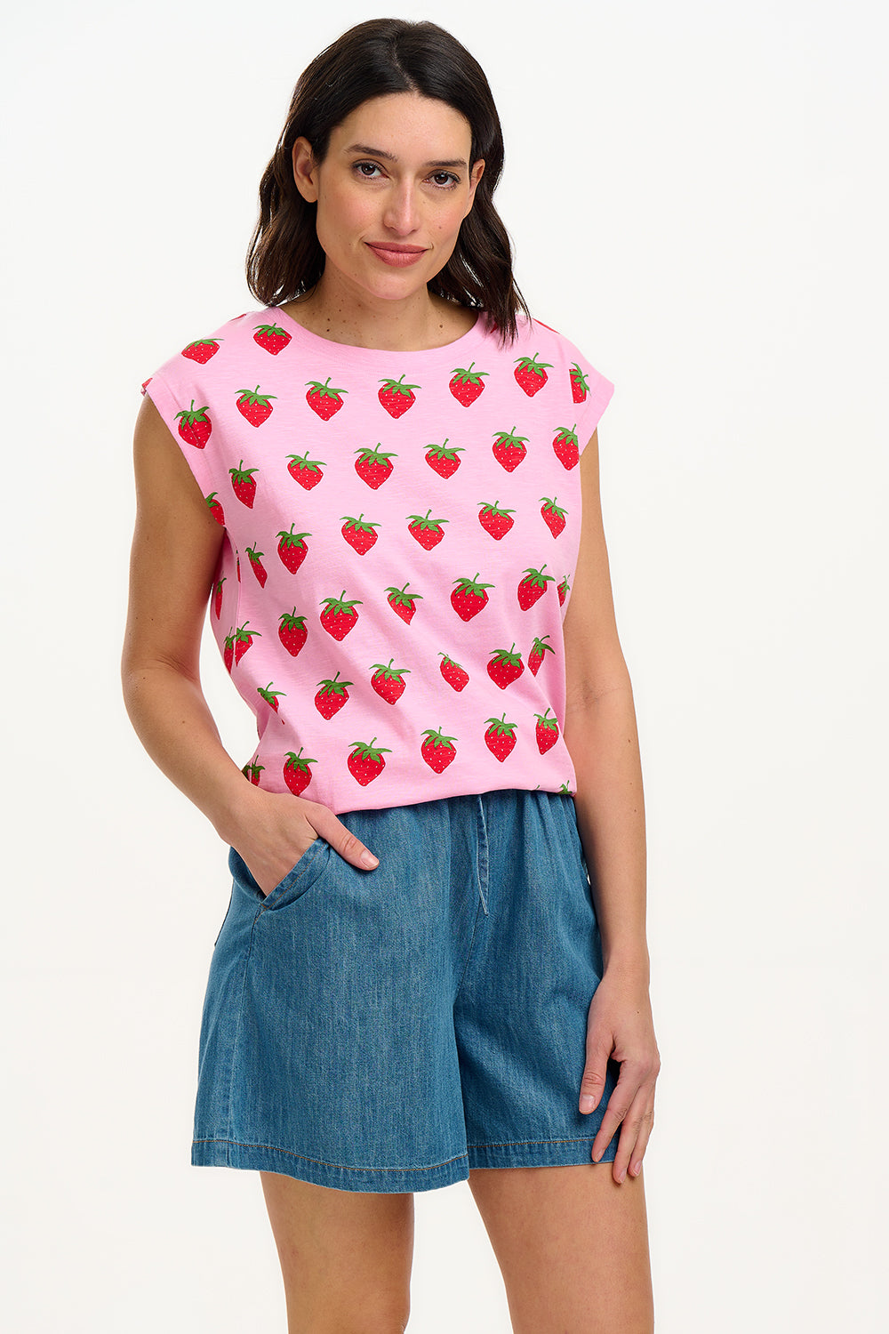 A model wearing a pink sleeveless tank top with a strawberry print, paired with blue denim shorts.
