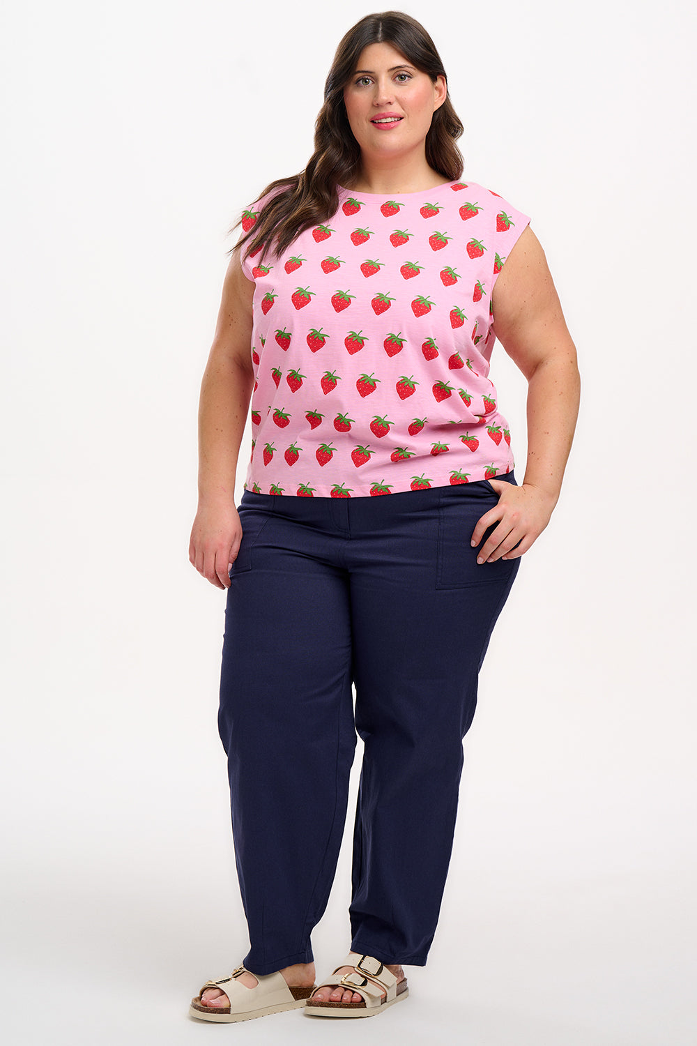 A model wearing a pink sleeveless tank top with a strawberry print, paired with blue jeans
