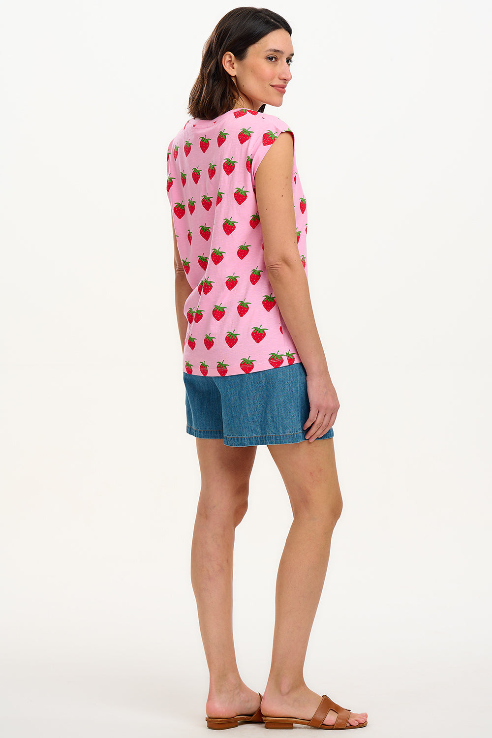 A model wearing a pink sleeveless tank top with a strawberry print, paired with blue denim shorts.