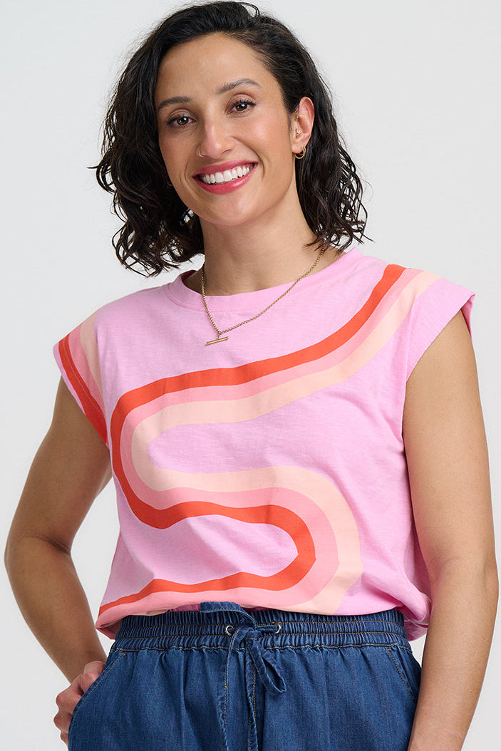 Woman wearing a pink sleeveless top with orange and blue design and blue shorts on a white background