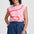 Woman wearing a pink sleeveless top with orange and blue design and blue shorts on a white background