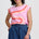 Woman wearing a pink sleeveless top with orange and blue design and blue shorts on a white background