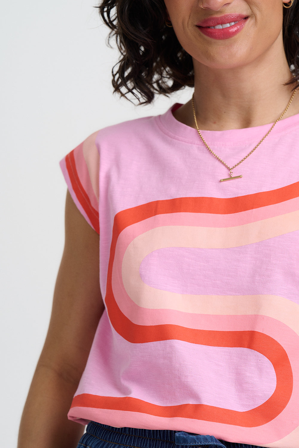 Woman wearing a pink sleeveless top with red and orange abstract design on a white background